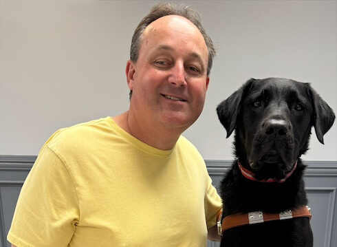 Bob sits next to black Lab guide dog Gage for team portrait