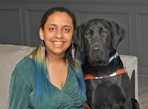 Angie smiles as she sits shoulder to shoulder with black Lab guide Douglas for the team portrait