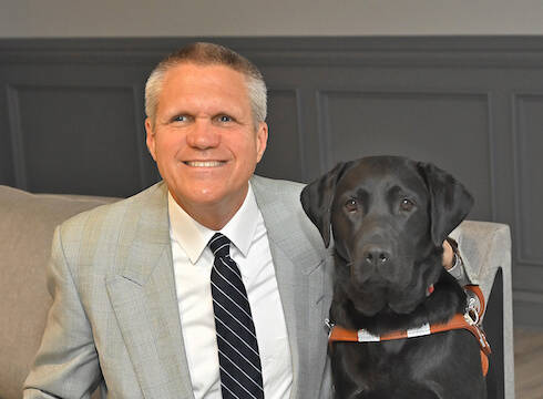 Joe and black lab guide dog Martha sit indoors for team portrait