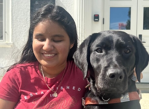 Daniela sits in a sunny area with her black Lab guide dog Sophie for their team portrait