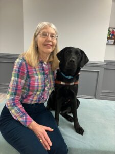 Deborah and black lab guide dog Giada sit for their team portrait.