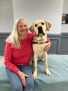 Moira sits with her arm around yellow lab Van who has head tilted slightly towards her