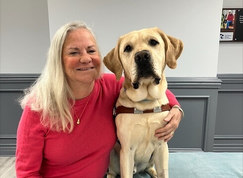 Moira sits with her arm around yellow lab Van who has head tilted slightly towards her