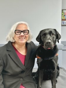 Jule Ann sits with black lab guide dog Stitch for their team portrait