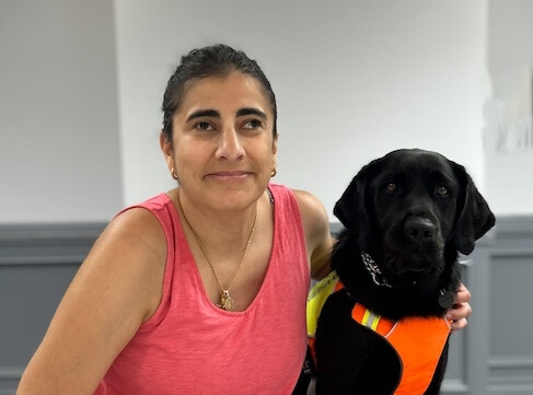 Ann and black lab guide dog Festiva sit together indoors for their team portrait