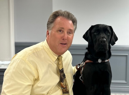 Donald and black lab guide dog Brandt sit together indoors for their team portrait