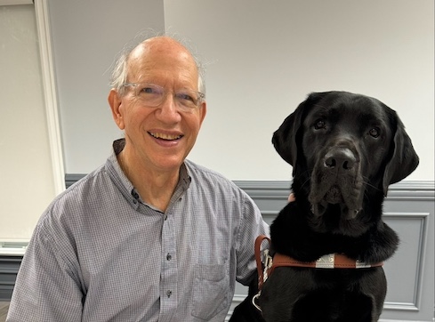 Alan sits beside his black Lab guide dog Forbes for their team portrait.