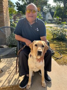 Latif sits outside with yellow lab guide dog Wyatt sitting at his feet for team portrait