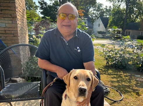 Latif sits outside with yellow lab guide dog Wyatt sitting at his feet for team portrait