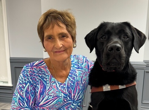 Linda sits beside her black Lab guide dog Watkins for their team portrait.