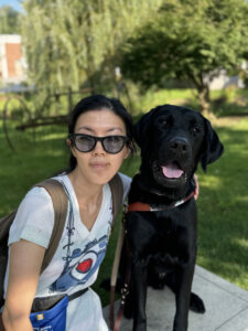 Yoojin and black lab guide Dennison sit close head to head as they sit on a bench