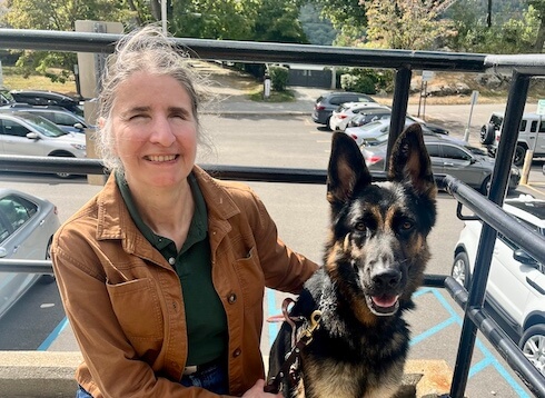 Elaine kneels next to German Shepherd Guide Dog Kenji on a landing overlooking a parking lot for their team portrait