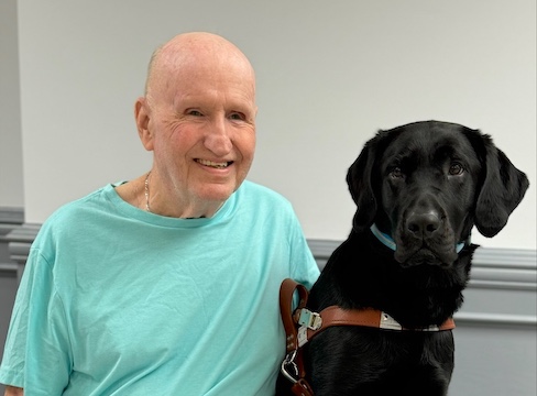 Mike and black Lab guide dog Dash sit side by side for their indoor team portrait