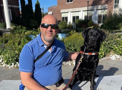 Timothy and black lab guide dog Magnus sit together on an outdoor bench for team portrait