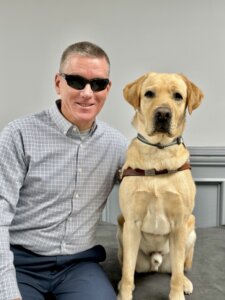 Ken and yellow Lab guide dog Paul sit side by side for their indoor team portrait