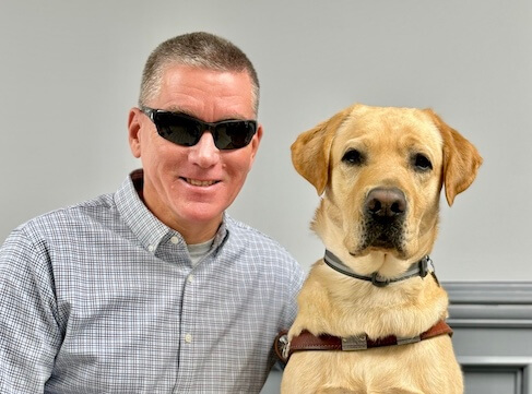 Ken and yellow Lab guide dog Paul sit side by side for their indoor team portrait