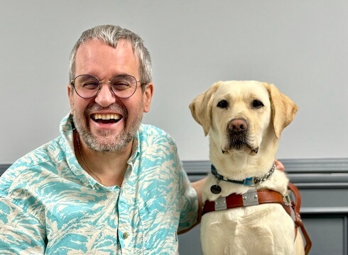 Richard and yellow Lab guide dog Baja sit side by side for their indoor team portrait