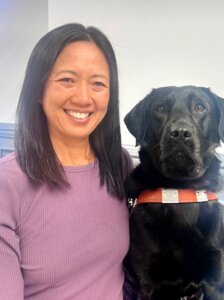 Terri sits with black lab guide dog Trinket for their team portrait