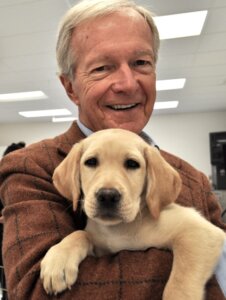 Bill Badger smiling while holding a yellow puppy at the Patterson facility