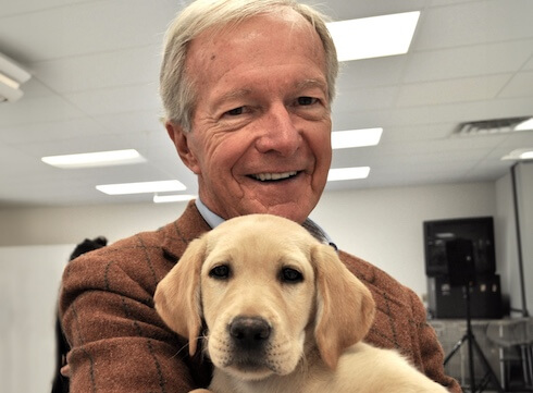 Bill Badger smiling while holding a yellow puppy at the Patterson facility