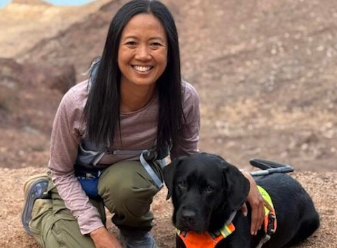 Terri Rupp sits back on her heels next to black guide dog Trinket at Zion National Park