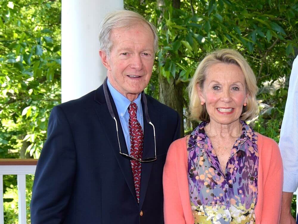 Bill Badger stands with his wife Sandie in front a white post and bright green foliage