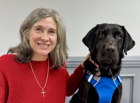 Carolyn sits with black Lab guide dog Yola for their team portrait