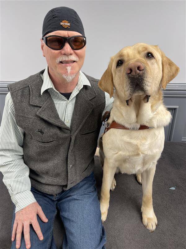 Lee and yellow Lab guide dog Nashville sit side by side for their indoor team portrait