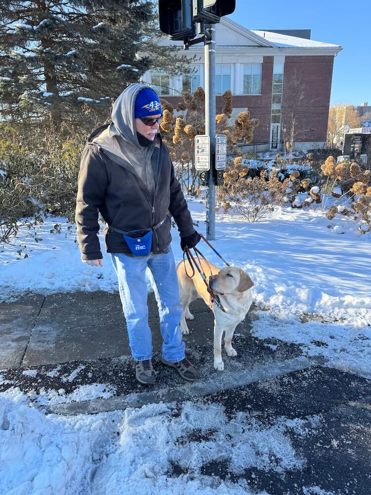 A bundled up Lee and guide dog Nashville check in with each other at a snowy curb