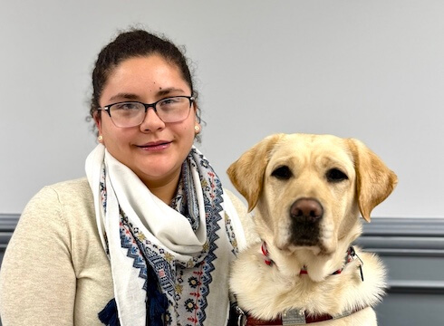 Viridiana and yellow Lab guide dog Quintessa sit side by side for their indoor team portrait