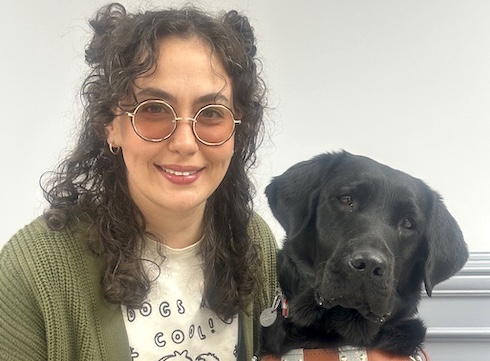 Izzy sits close to black Lab guide dog Bright indoors for their team portrait