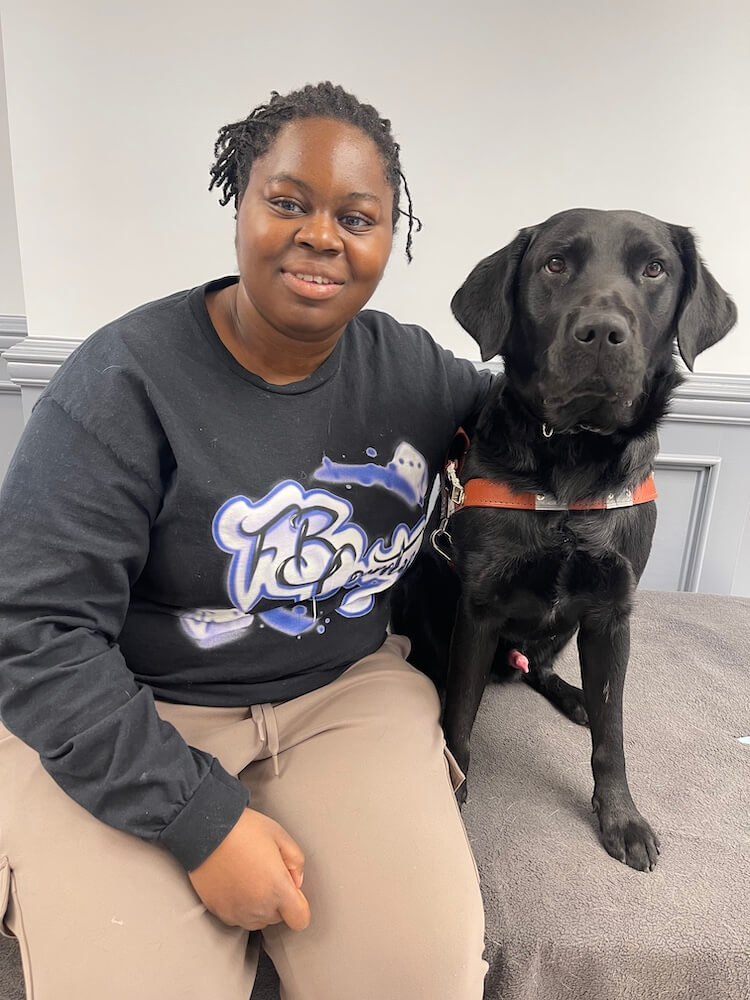 Osolu and black Lab guide dog Cliff sit side by side for their indoor team portrait