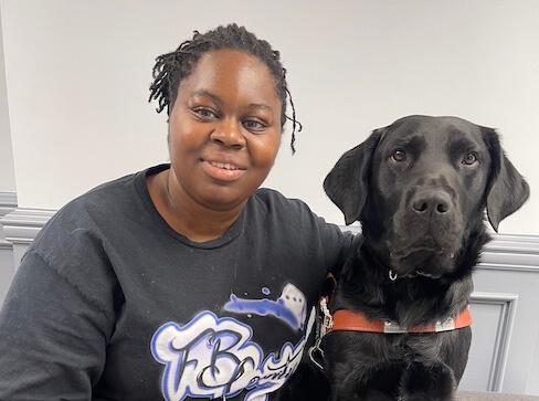 Osolu and black Lab guide dog Cliff sit side by side for their indoor team portrait